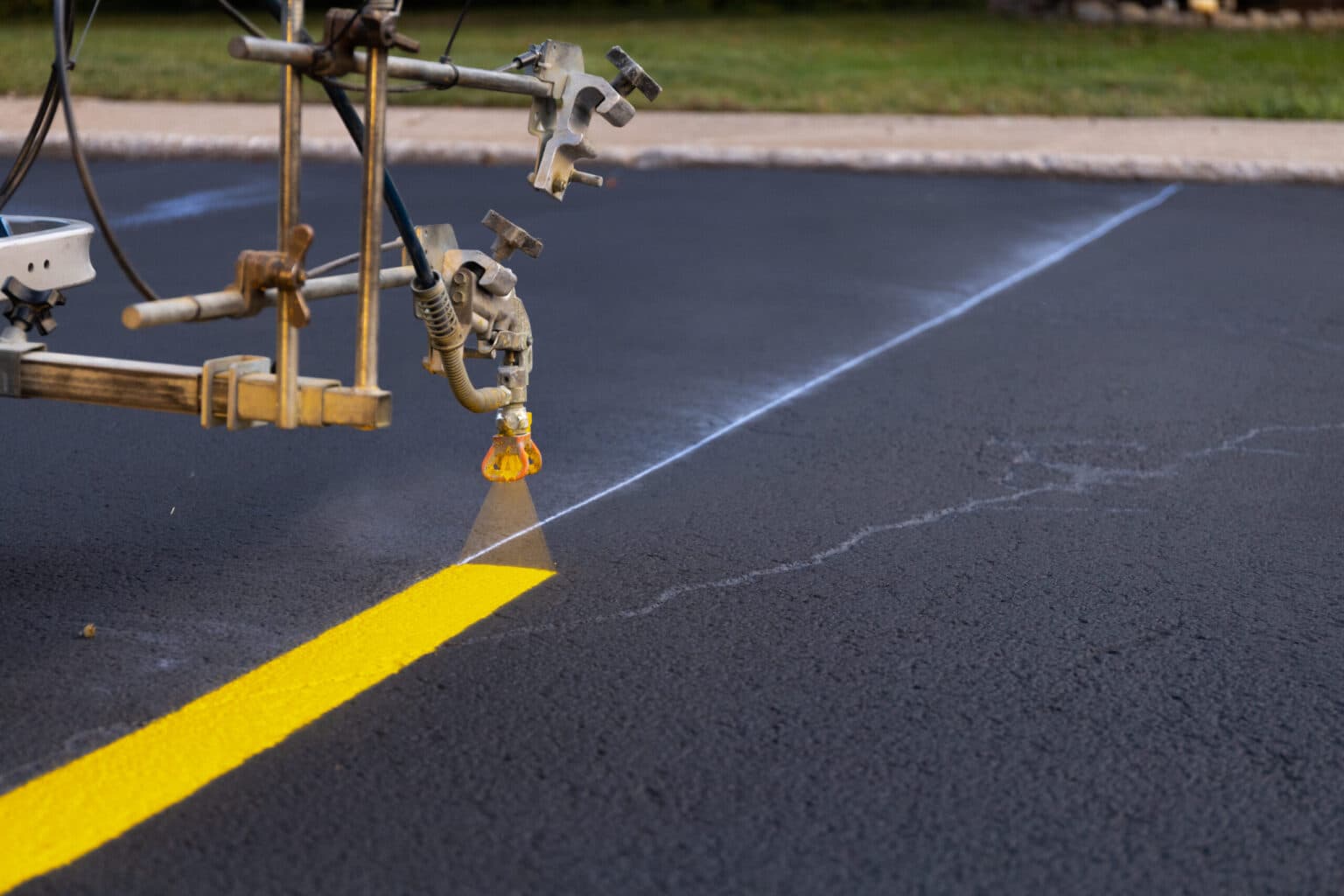 Striping machine spraying a fresh yellow line onto newly paved asphalt